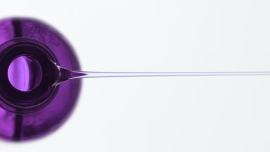 Bakuchoil is being poured from purple bottle on grey background