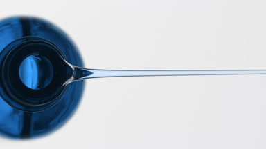 Blue reagent bottle is being tilted and blue oil pours from it