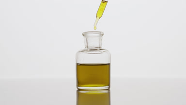 Dropper drips yellow oil into reagent bottle on grey background