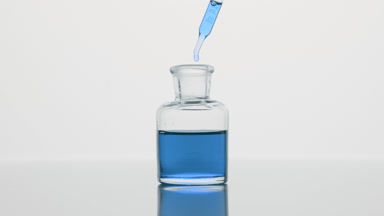 Dropper drips blue oil into reagent bottle on grey background