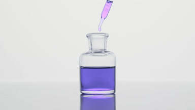Dropper drips purple oil into reagent bottle on grey background