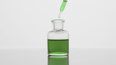 Dropper drips green oil into reagent bottle on grey background