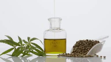 Hemp oil pouring in bottle near hemp sprig and scoop with seeds