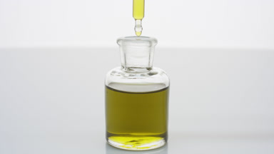 Lab dropper drips yellow fluid into bottle on grey background