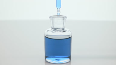 Lab dropper drips cyan fluid into bottle on grey background