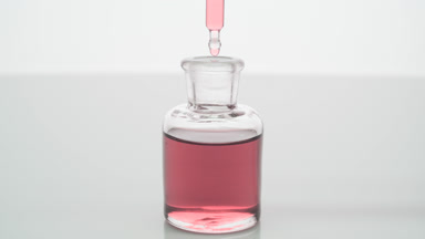 Lab dropper drips pink fluid into bottle on grey background