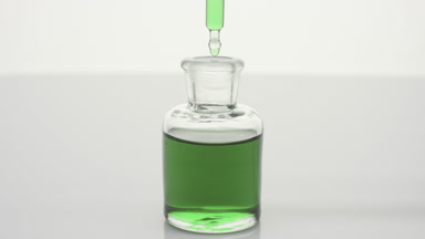 Lab dropper drips green fluid into bottle on grey background