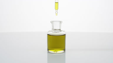 Lab dropper drips chamomile oil into bottle on grey background