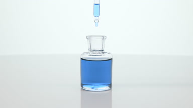 Lab dropper drips blue tansy oil into bottle on grey background