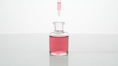 Lab dropper drips rose water into bottle on grey background
