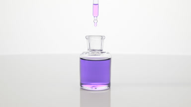 Lab dropper drips lavender oil into bottle on grey background