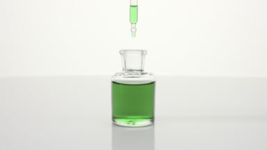 Lab dropper drips green tea oil into bottle on grey background