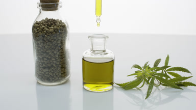 Dropper drips oil into bottle near glass seed jar and hemp sprig
