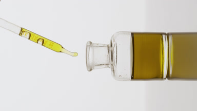 Pipette drips yellow oil into reagent bottle on grey background