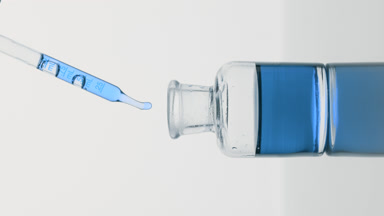 Pipette drips cyan oil into reagent bottle on grey background