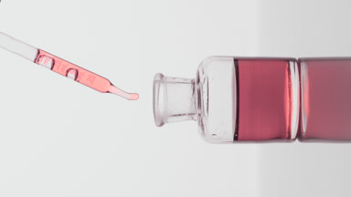 Pipette drips rose oil into reagent bottle on grey background