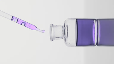 Pipette drips violet oil into reagent bottle on grey background