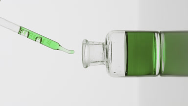 Pipette drips green oil into reagent bottle on grey background