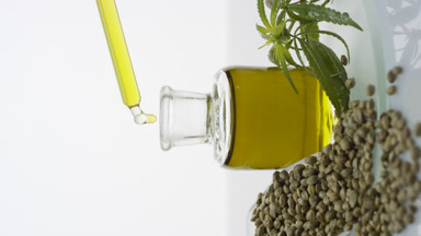Pipette drips oil in bottle on glass with seeds scoop and sprig
