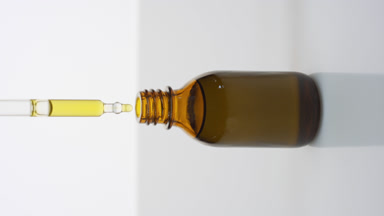 Dropper drips yellow oil into brown bottle on grey background