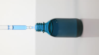 Dropper drips blue oil into blue bottle on grey background