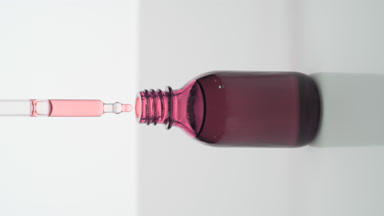 Dropper drips pink oil into pink bottle on grey background