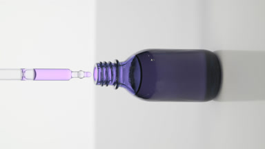 Dropper drips purple oil into purple bottle on grey background
