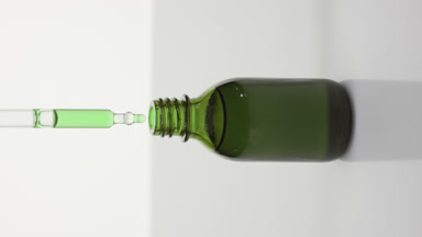 Dropper drips green oil into green bottle on grey background
