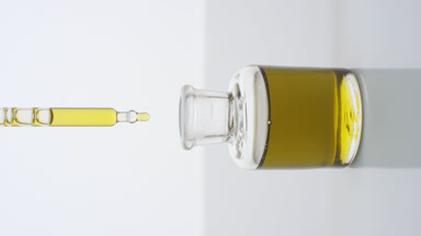 Lab dropper drips yellow liquid into bottle on grey background