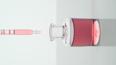 Lab dropper drips pink liquid into bottle on grey background
