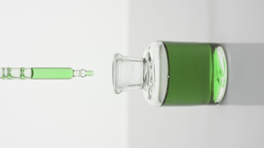 Lab dropper drips green liquid into bottle on grey background