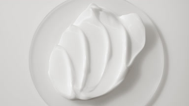 Extreme close-up jib shot of white cosmetic cream on glass round