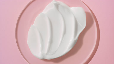 Crane shot of white cream on glass round on pale pink background