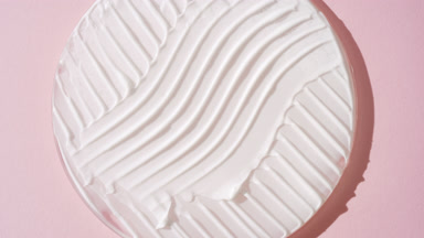 Crane shot of white cream on glass round on pale pink background
