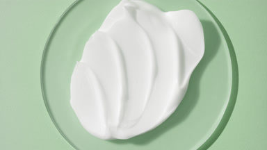Jib shot of white day cream on glass round on green background