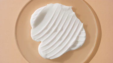Jib shot of white cream on watch glass round on beige background