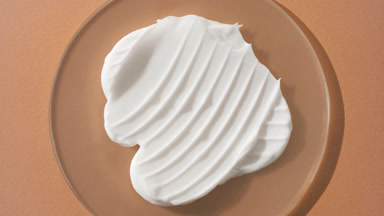 Crane shot of white day cream on watch glass on beige background