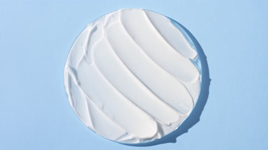White anti-aging cream on watch glass on pale blue background