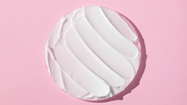 White anti-aging cream on watch glass on pale pink background
