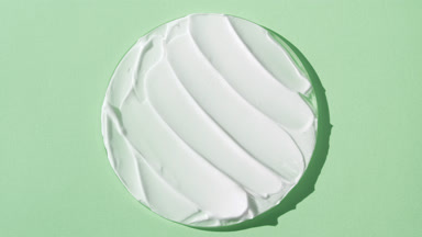 White anti-aging cream on watch glass on green background