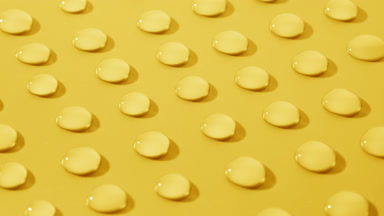 Side view macro of moving transparent drops on yellow background