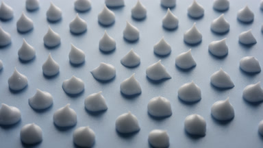 Jib shot of drops of white cream on blue background in shadow