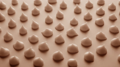 Jib shot of drops of beige cream on beige background in shadow