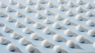 Multiple drops of white cream on pale blue background
