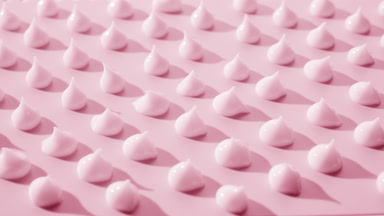 Multiple drops of pink cream on pale pink background