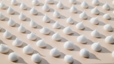 Multiple drops of white cream on beige background