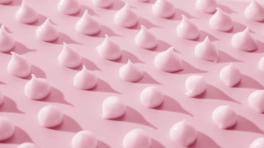 Multiple drops of pink day cream on pink background