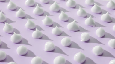 Multiple drops of white day cream on purple background