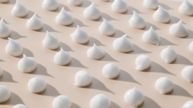 Multiple drops of white day cream on beige background