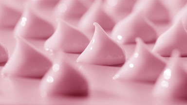 Macro of multiple drops of pink day cream on pink background